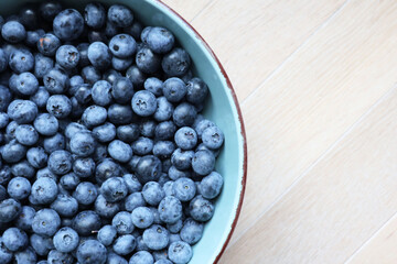 Fresh ripe blueberries in a light blue ceramic bowl on a wooden surface