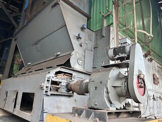The image shows a large industrial furnace or boiler with an intricate feeding mechanism and a prominent electric motor. The machinery appears aged and heavily used, highlighting a heavy-duty factory 