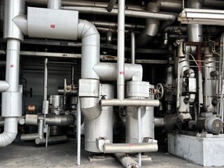 a complex tangle of industrial pipes, valves, and machinery within a factory. The scene highlights the dense and intricate infrastructure used for processing and production in a heavy industry setting