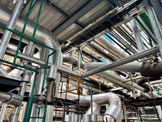 This photo depicts a complex, overhead industrial network of large pipes and machinery, highlighting the intricate and dense infrastructure found in a modern factory or processing plant.