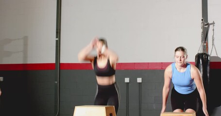 Performing plyometric box jumps under trainer cue female workout partners building strength in gym - Powered by Adobe