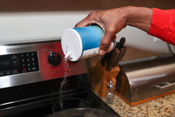 A black man pouring salt on food with the concept of high blood pressure 