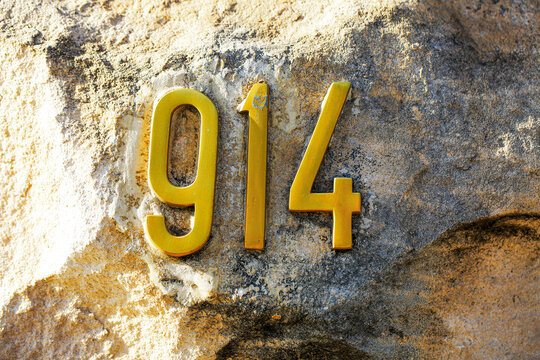 House number 914 displayed with golden metallic numerals mounted on a natural stone wall. Yellow digits contrast with rough rock texture, concept of address signage, property marker