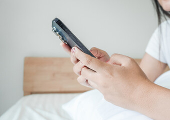 Close up hand holding phone browsing internet in bedroom, chatbot, remote work or freelance and online shopping. Woman using phone sleeping in bed at home. Female use smartphone in house or apartment 