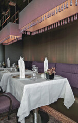 Formal and elegant a la carte ocean view dining room restaurant onboard luxury cruiseship or cruise ship liner with set tables in modern purpl wood creme Art Deco interior design style ambient light