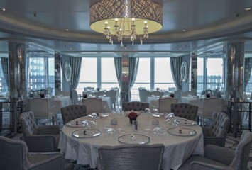 Formal and elegant a la carte ocean view dining room restaurant onboard luxury cruiseship or cruise ship liner with set tables in modern grey white silver Art Deco interior design style ambient light