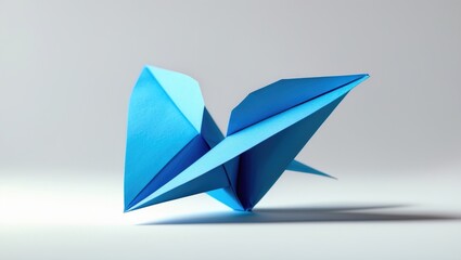 Fototapeta premium Blue origami bird with wings spread, made from paper, on a plain white background.