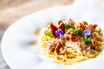 Gourmet spaghetti with meat, sun-dried tomatoes, parsley, and edible flowers on a white plate. Vibrant, artistic food presentation with shallow depth of field