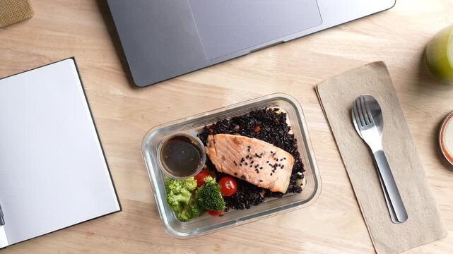 Top view of person eating Salmon and Riceberry meal prep while working at desk