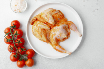 Raw marinated quail on white plate with tomatoes, salt, pepper and rosemary
