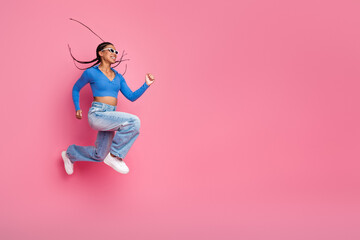 Energetic young woman in stylish casual outfit leaping joyfully against a vibrant pink background showcasing positivity