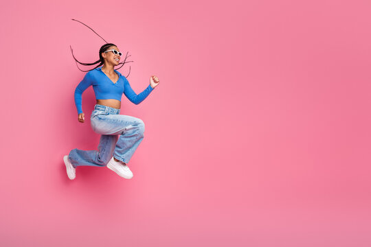 Energetic young woman in stylish casual outfit leaping joyfully against a vibrant pink background showcasing positivity