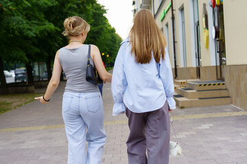 Fototapeta premium Two friends walking side by side on a tree-lined street in a modern urban area during late afternoon