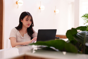 Asian woman freelancer works online laptop computer modern cafe coffee shop digital nomad productive focused remote work study bright workspace