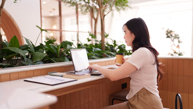 Asian adult woman remote work laptop modern cafe managing freelance business tasks enjoying coffee drink