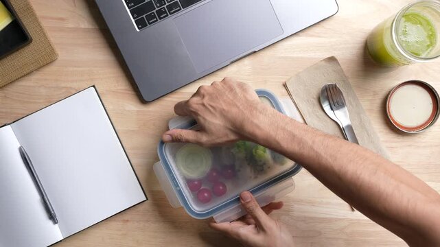 Top view of person eating Salad Wrap meal prep container on the office desk.