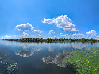 Clouds are reflected in the river. Puffs of steam hover over the surface of the water. Landscape with sky and waves. Freshwater reserves. Water lilies overgrow the surface. Day blue sky.
