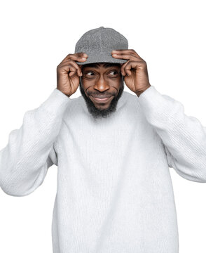A man with a beard, wearing a white sweater, tries to put on a cap while looking to the side with a playful expression, isolated on a transparent background.