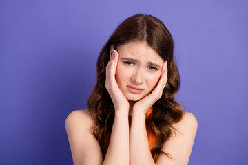 Lovely young woman in a casual orange top feeling contemplative while posing against a vibrant purple backdrop
