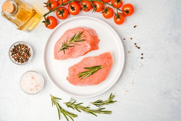 Two raw veal steaks with rosemary on white plate surrounded by cooking spices and vegetables