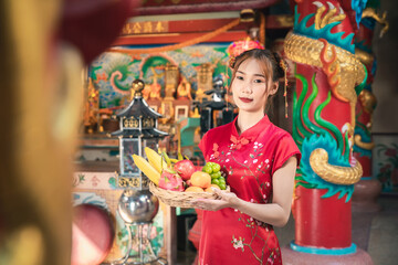 Portrait of young Chinese woman in red cheongsam qipao dress holding a fruit basket for worshipped...