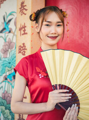 Obraz premium Portrait young Asian woman in traditional cheongsam qipao dress holding fan in her hand at Chinese temple. Chinese new year concept.