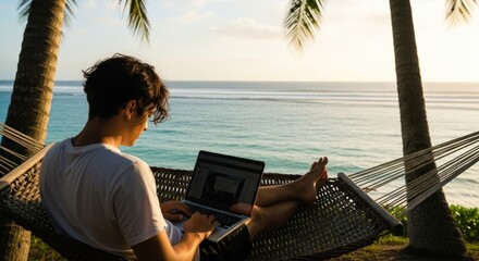 A man in a white t-shirt lounges in a hammock by the ocean, using a laptop.
