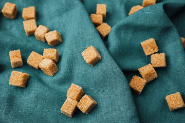 Sweet and natural brown sugar cubes scattered on dark green fabric