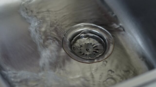 Water drain down on stainless steel kitchen sink hole, cleaning and hygiene concept.