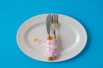 Fork and knife with Measuring tape around on white dishes.Health concept.