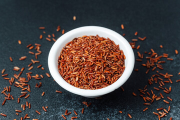 Close up of red rice in white bowl with scattered grains