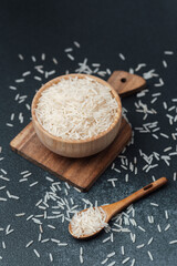 White rice in wooden bowl with scattered grains and wooden spoon