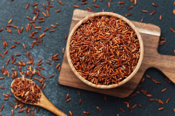 Red rice in wooden bowl on cutting board with scattered grains and spoon