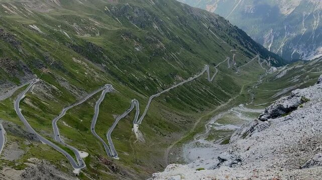 A panoramic view of the winding mountain roads of the famous Stelvio Pass, set against a backdrop of majestic peaks and a cloudy sky.