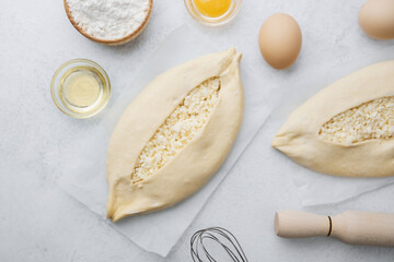 Two raw khachapuri with cheese and eggs on light surface with ingredients