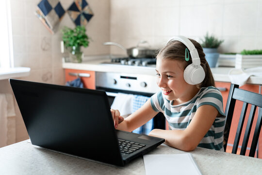 Happy school girl in headphones using laptop at home for online lesson in virtual class, video call. Remote education for child, homeschooling, e-learning. Technology lifestyle, coding for kid