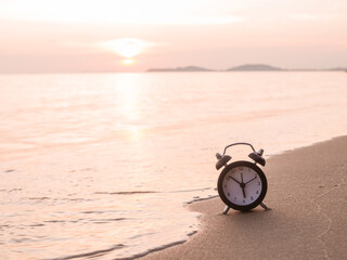 Fototapeta premium Black alarm clock on the beach in the sunset time. The concept about Time to summer, Travel, Vacation and Relaxation