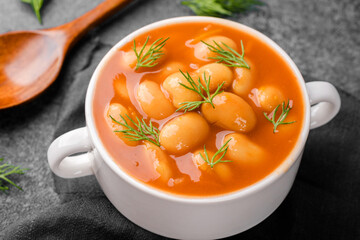 Baked beans in tomato sauce with dill in white bowl on black surface for vegan, comfort food or...