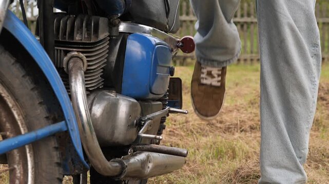 Mechanic starting old motorcycle engine with kick starter