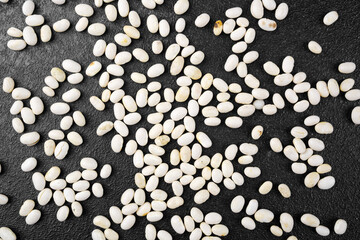 Scattered white beans on dark stone background for texture, vegan food or background pattern concept