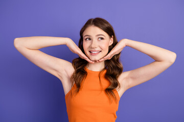 Fototapeta premium Beautiful young woman in orange tank top posing with cheerful smile against violet background in a stylish casual theme