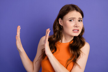Fototapeta premium Lovely young woman expressing hesitation against bright purple backdrop, capturing emotions and casual style in her bright orange top