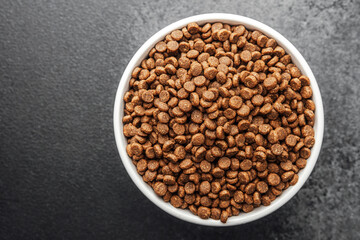 White bowl with dry dog food on dark gray background