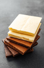 Stack of assorted chocolate pieces in white, milk and dark flavors on black background