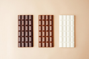 Assorted chocolate bars in dark milk and white varieties on beige background