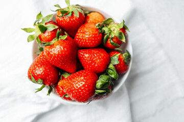 Fresh strawberries in a white bowl on a light background during daylight hours