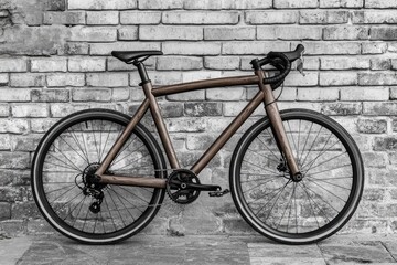 A wooden-framed bicycle stands against a weathered brick wall, showcasing unique craftsmanship and a blend of classic and modern design elements.