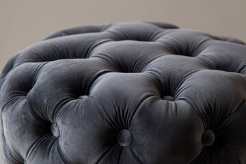 Close-up shot of a stylish, charcoal-colored, velvet-upholstered ottoman with tufted detailing and a neutral background, perfect for interior design.