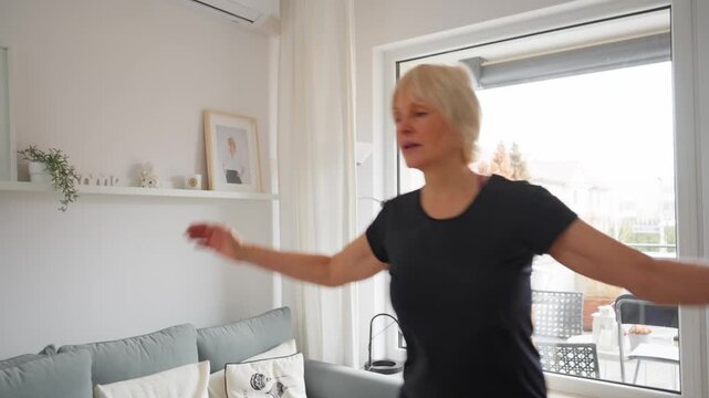An active senior performs a safe, low-impact cardio routine at home. She combines side-steps with rhythmic arm movements, clapping her hands in front of her to stay fit.
