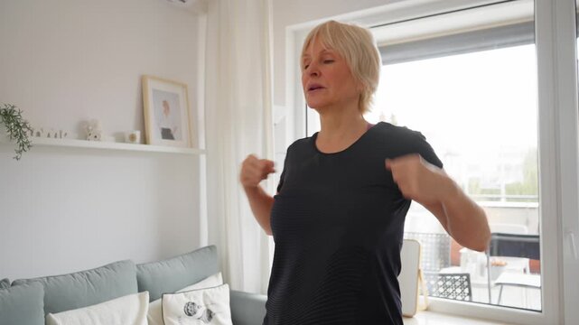 Fit senior woman practicing wellness gymnastics and warm-up exercises at home. Active pensioner enjoying a healthy lifestyle, training for longevity and vitality with physiotherapy movements.